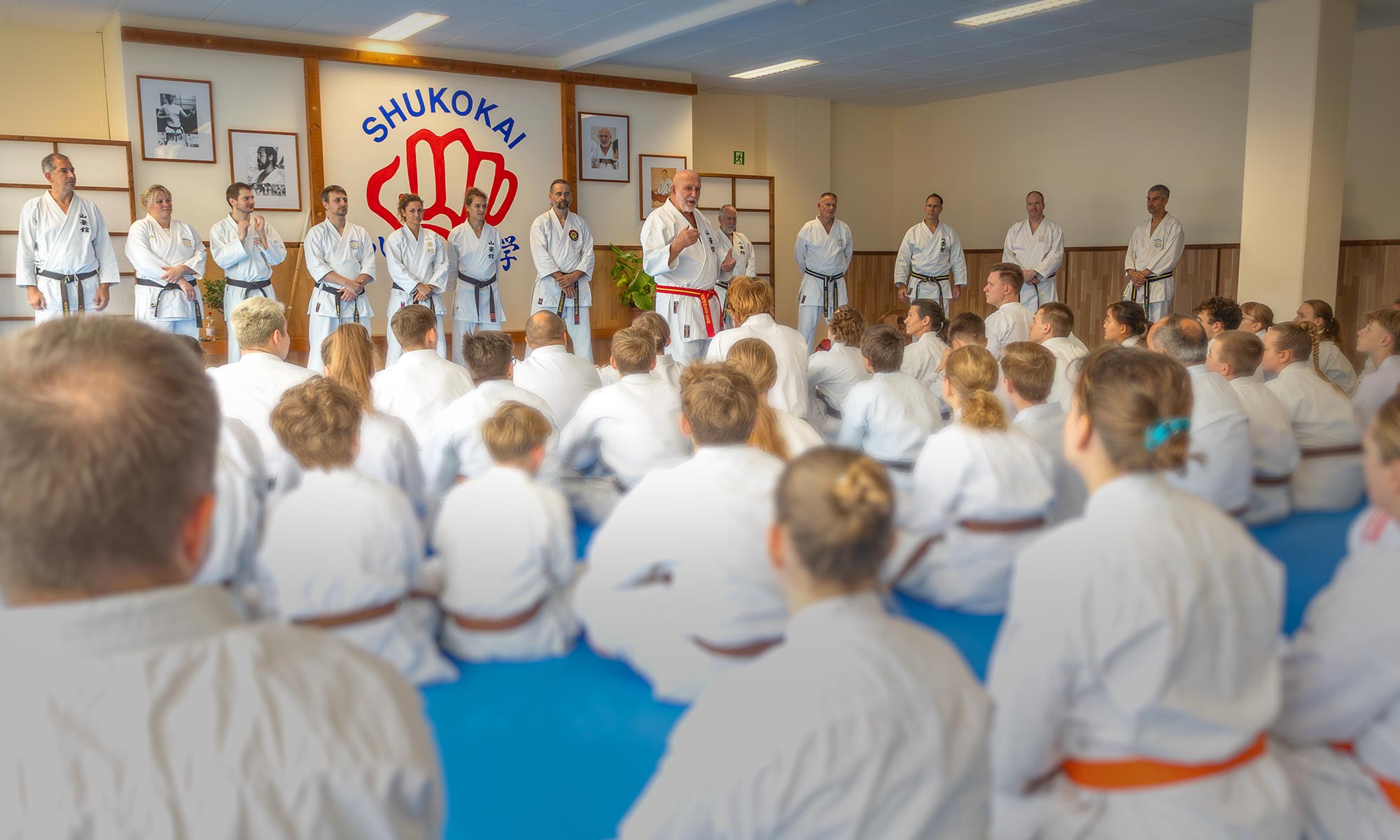 Seminar in the dojo: instructors and students in karate gi in front of the Shukokai emblem